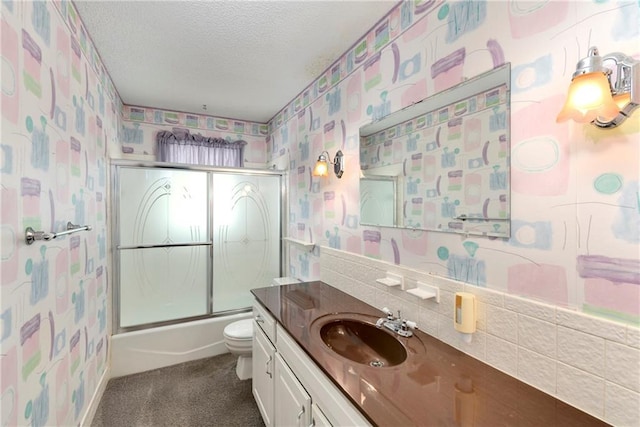 full bathroom featuring wallpapered walls, a textured ceiling, toilet, vanity, and combined bath / shower with glass door