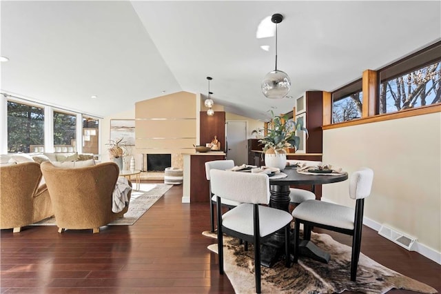 dining area featuring dark wood-type flooring, a fireplace with raised hearth, visible vents, lofted ceiling, and baseboards