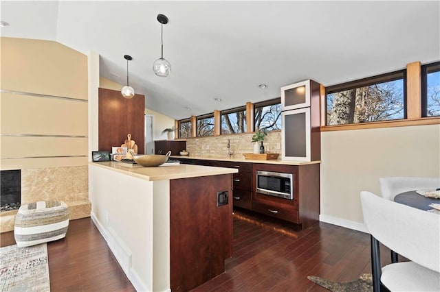 kitchen with a sink, light countertops, dark wood-style floors, stainless steel microwave, and decorative backsplash