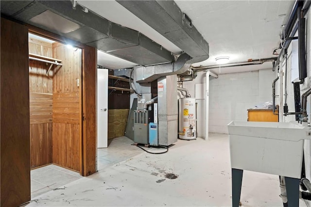 unfinished basement featuring concrete block wall, a sink, gas water heater, and heating unit