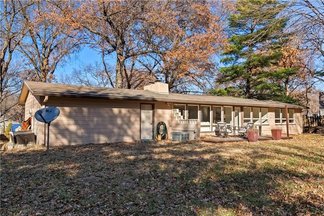 rear view of property featuring a sunroom, a chimney, and a lawn