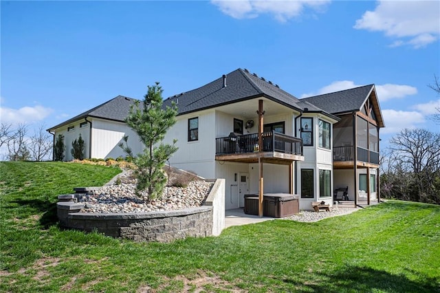 rear view of property with roof with shingles, a lawn, a patio area, a hot tub, and a balcony