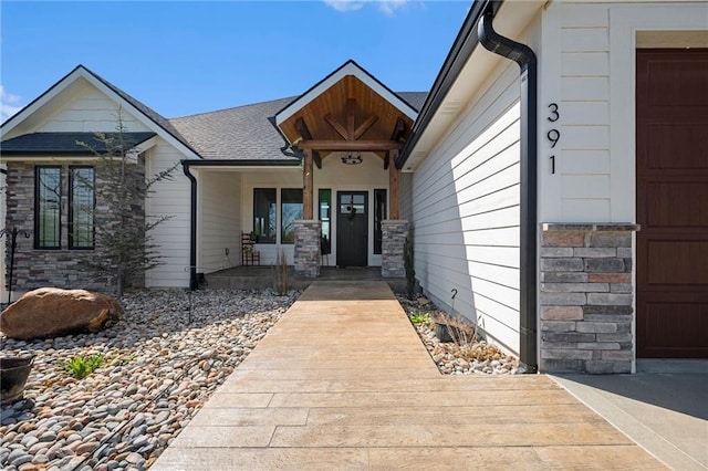 entrance to property featuring a garage, covered porch, a shingled roof, and stone siding