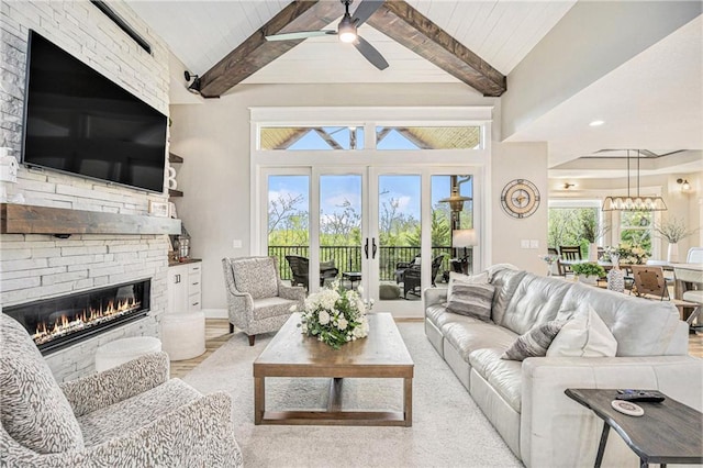 living area with wood finished floors, a stone fireplace, baseboards, lofted ceiling with beams, and ceiling fan with notable chandelier