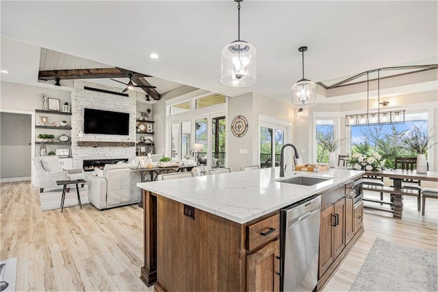 kitchen with a kitchen island with sink, stainless steel dishwasher, a sink, lofted ceiling with beams, and light wood-style floors