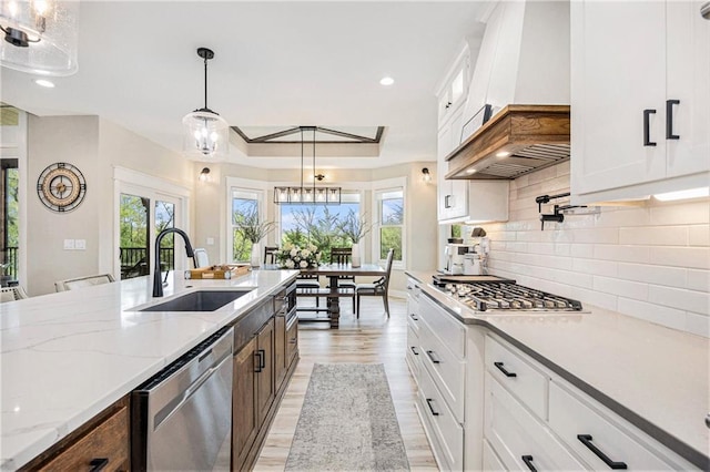 kitchen with pendant lighting, appliances with stainless steel finishes, a sink, white cabinets, and light wood-style floors