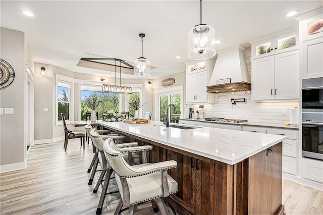 kitchen featuring appliances with stainless steel finishes, a sink, a kitchen island with sink, decorative backsplash, and custom range hood