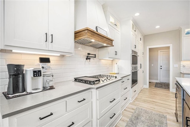 kitchen with glass insert cabinets, white cabinetry, tasteful backsplash, custom range hood, and appliances with stainless steel finishes