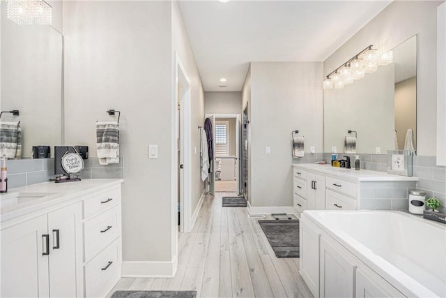 bathroom with wood finished floors, baseboards, two vanities, a sink, and backsplash