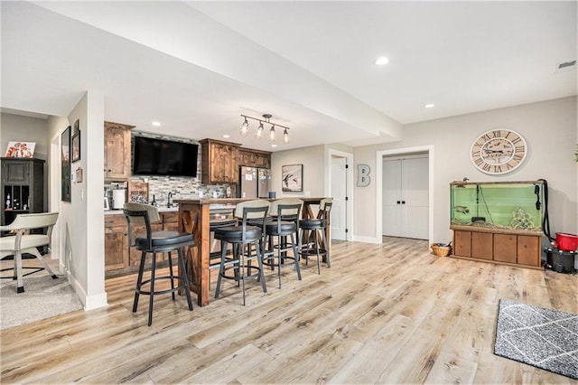 kitchen with decorative backsplash, baseboards, freestanding refrigerator, a breakfast bar, and light wood-style flooring