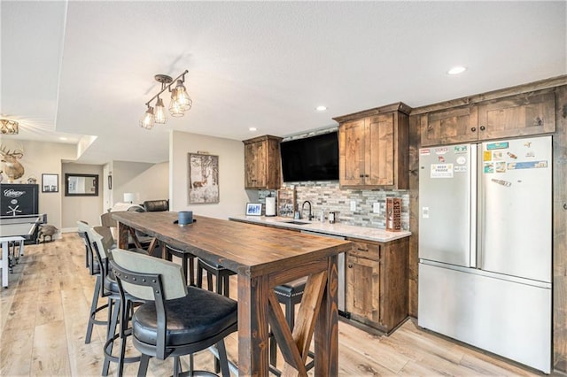 kitchen with backsplash, a sink, light countertops, freestanding refrigerator, and light wood-style floors
