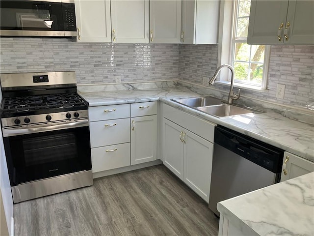 kitchen with appliances with stainless steel finishes, a sink, white cabinets, wood finished floors, and light stone counters