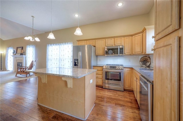 kitchen with tasteful backsplash, light stone countertops, light brown cabinetry, appliances with stainless steel finishes, and a kitchen bar