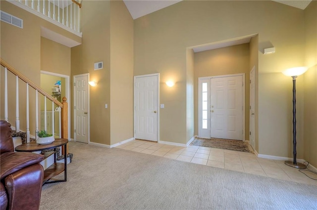 carpeted foyer with high vaulted ceiling, tile patterned floors, and visible vents