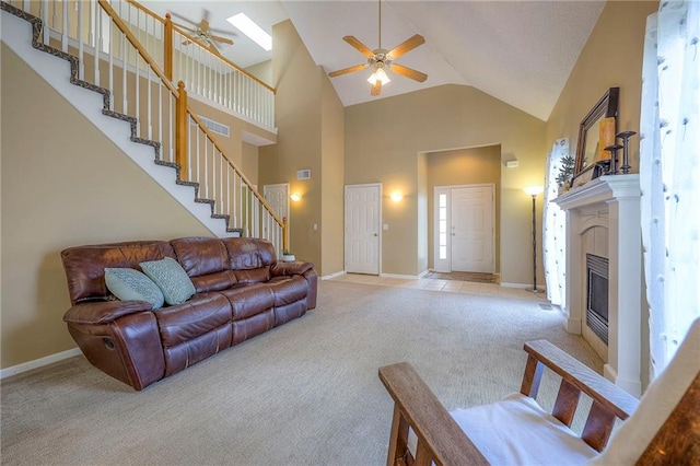 living area with light colored carpet, stairway, a glass covered fireplace, a ceiling fan, and high vaulted ceiling