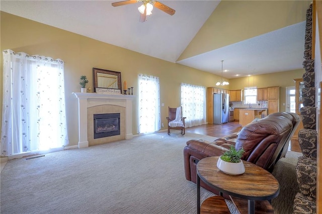 living room with a tile fireplace, visible vents, light colored carpet, lofted ceiling, and ceiling fan with notable chandelier