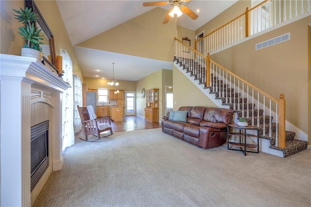 carpeted living area with a tile fireplace, visible vents, high vaulted ceiling, and stairs