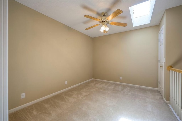spare room with baseboards, a skylight, ceiling fan, and light colored carpet