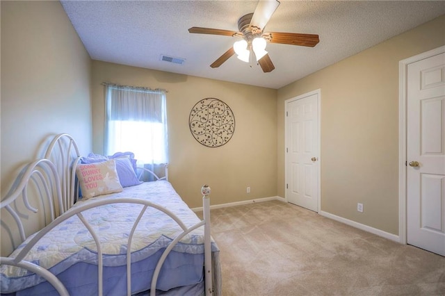 bedroom with a textured ceiling, visible vents, a ceiling fan, and light carpet