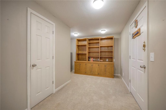 hall with a textured ceiling, light colored carpet, and baseboards