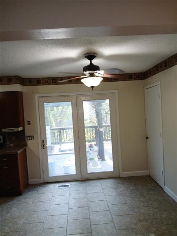 entryway with a textured ceiling, ceiling fan, light tile patterned flooring, and baseboards