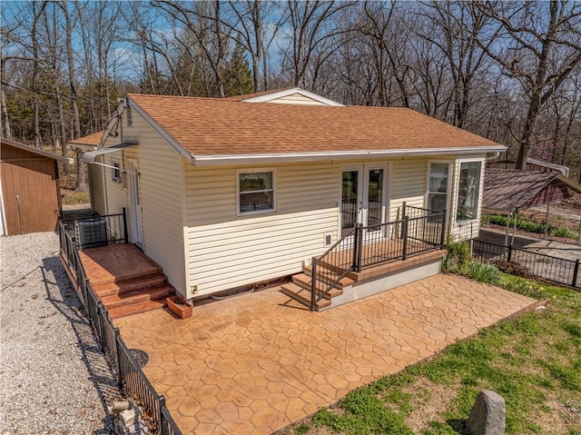 exterior space featuring a patio area, french doors, fence, and a shingled roof