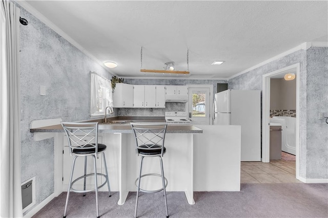 kitchen with white appliances, a peninsula, a textured ceiling, white cabinets, and light carpet