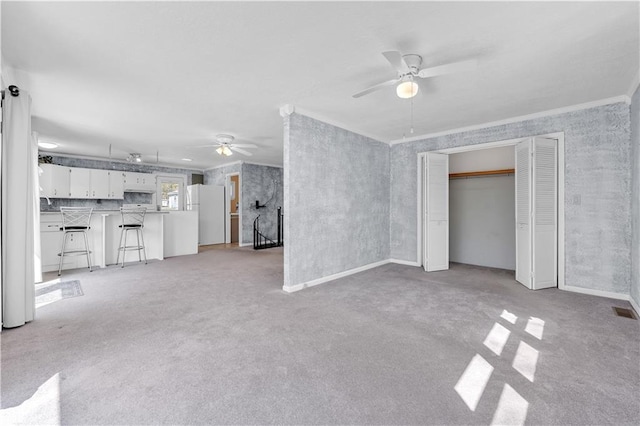 unfurnished living room featuring light carpet, visible vents, a ceiling fan, and crown molding