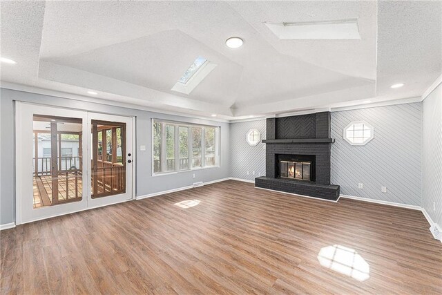 710 N Redwood Dr, Independence, MO 64056 - unfurnished living room featuring baseboards, a skylight, wood finished floors, a fireplace, and a raised ceiling