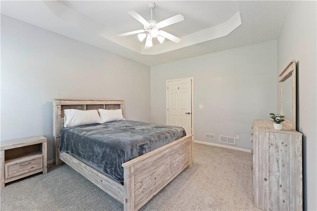 bedroom with carpet flooring, visible vents, a tray ceiling, and ceiling fan