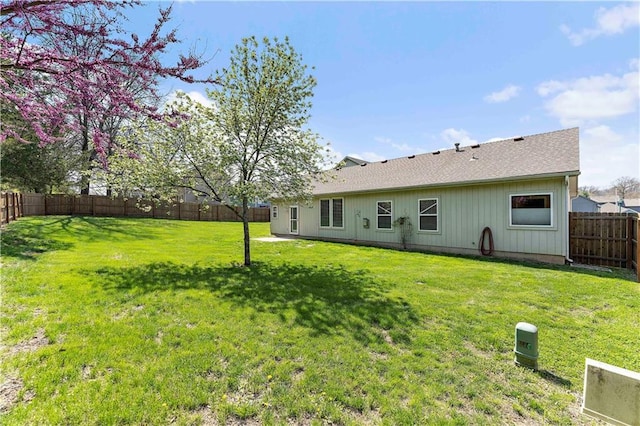 rear view of house featuring a fenced backyard, a lawn, and roof with shingles