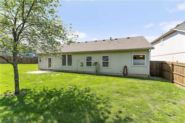 rear view of property featuring a shingled roof, a fenced backyard, and a lawn