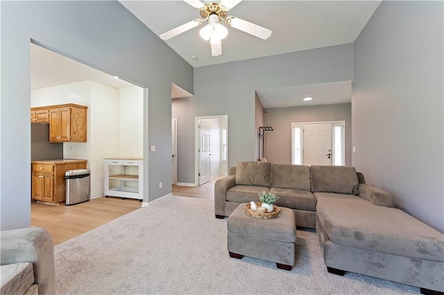 living room featuring baseboards, a high ceiling, a ceiling fan, light wood-style flooring, and light carpet