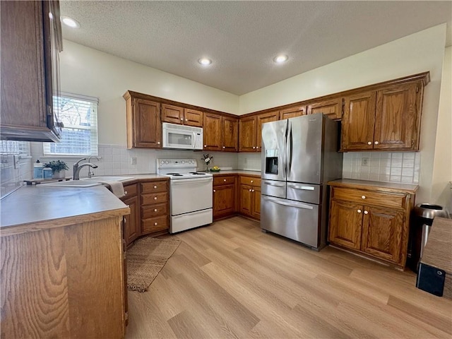 kitchen featuring light wood-style floors, brown cabinets, white appliances, and a textured ceiling