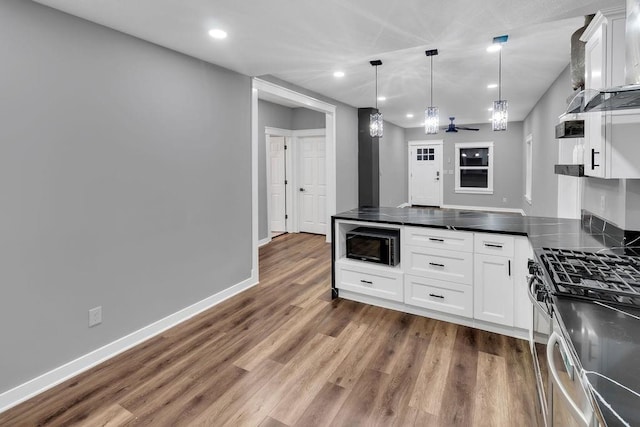 kitchen featuring stainless steel gas range, dark countertops, black microwave, recessed lighting, and wood finished floors