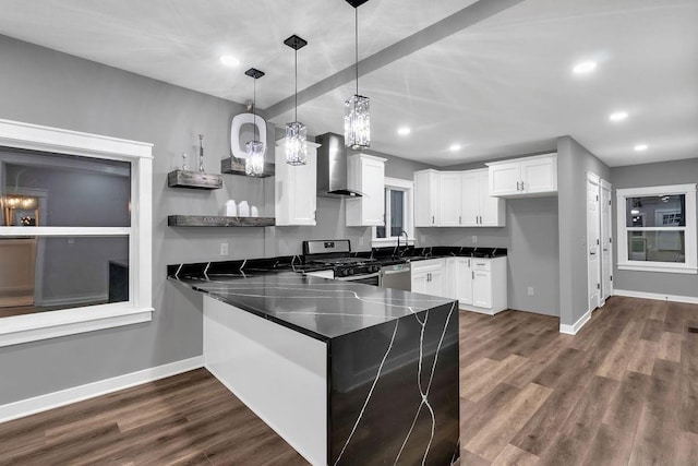 kitchen with a peninsula, appliances with stainless steel finishes, wall chimney exhaust hood, and baseboards
