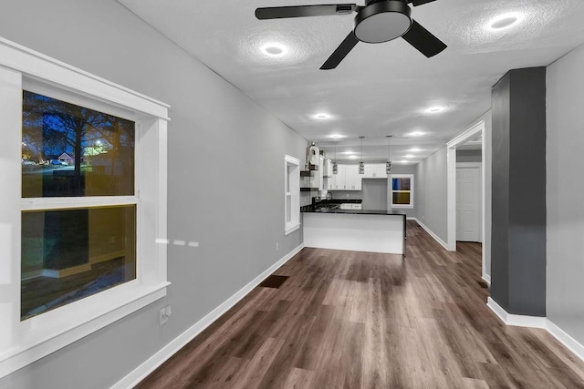 unfurnished living room featuring dark wood-type flooring, a textured ceiling, baseboards, and a ceiling fan