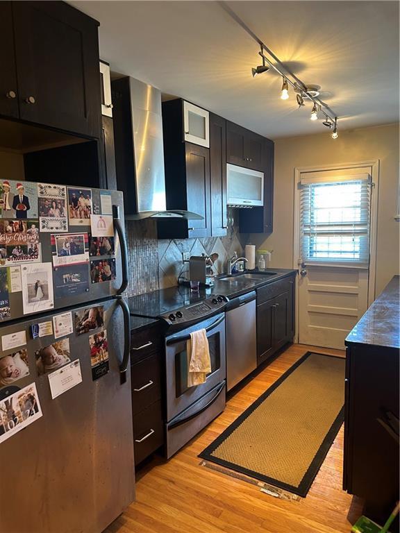 4209 Clark Ave Unit 4209-4, Kansas City, MO 64111 - kitchen featuring wall chimney exhaust hood, a sink, light wood-type flooring, dark cabinets, and stainless steel appliances