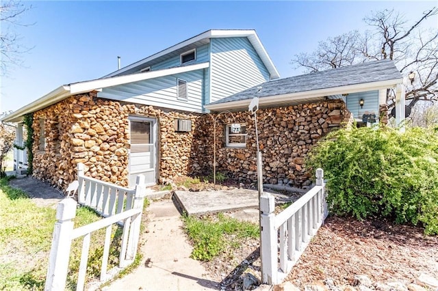 view of side of property with fence, stone siding, and a shingled roof