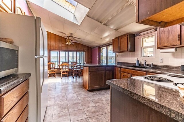 kitchen featuring stainless steel microwave, a peninsula, dark countertops, lofted ceiling with skylight, and a sink