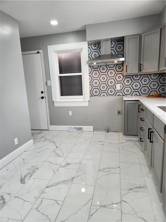 kitchen with wall chimney exhaust hood, gray cabinets, marble finish floor, light countertops, and baseboards