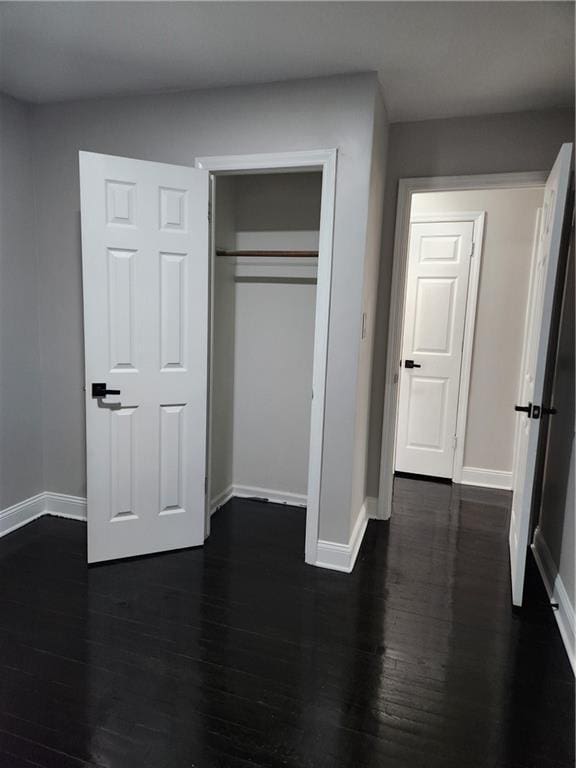 unfurnished bedroom with a closet, baseboards, and dark wood-style floors