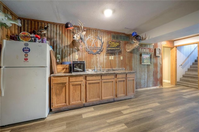 43 901st Rd, Clinton, MO 64735 - kitchen with freestanding refrigerator, brown cabinetry, light wood-type flooring, wooden walls, and baseboards