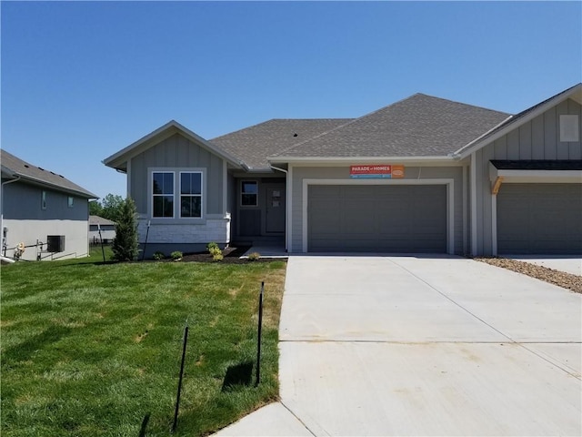 4967 146th St, Basehor, KS 66007 - view of front of property with board and batten siding, a front yard, driveway, an attached garage, and roof with shingles
