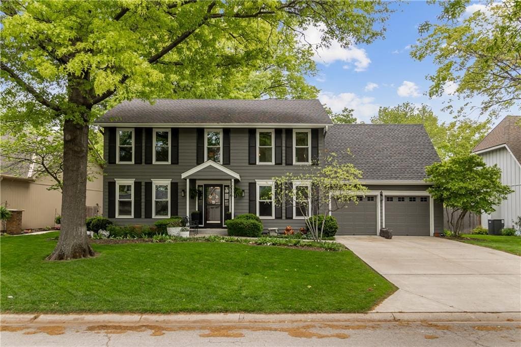 colonial inspired home featuring an attached garage, driveway, and a front lawn