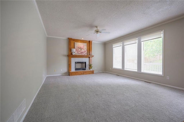 unfurnished living room featuring ornamental molding, ceiling fan, a textured ceiling, a tiled fireplace, and carpet floors