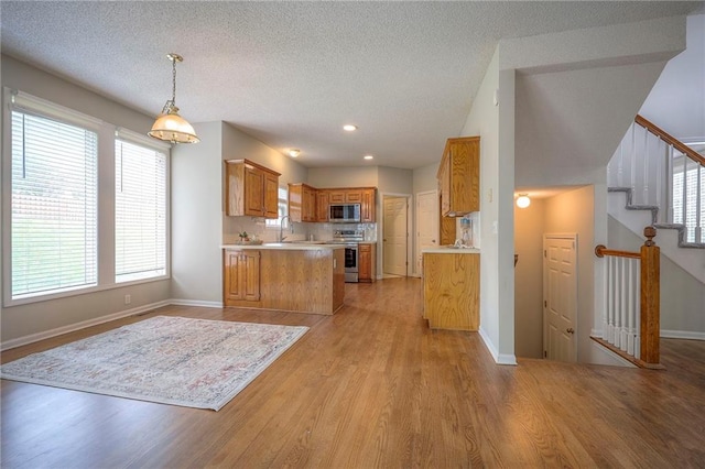 kitchen featuring appliances with stainless steel finishes, light countertops, brown cabinets, a sink, and baseboards