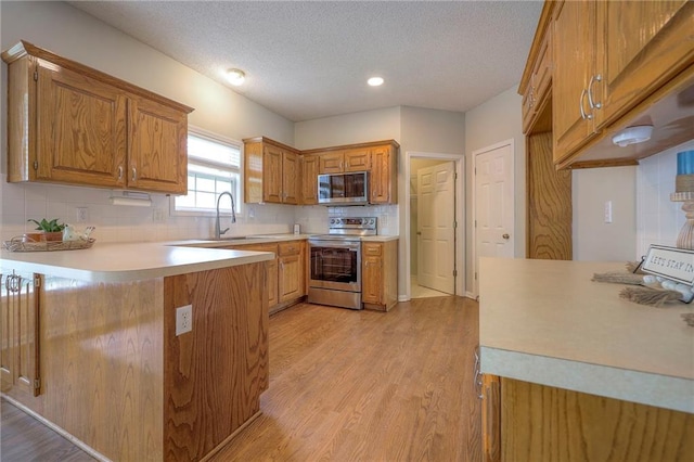 kitchen with appliances with stainless steel finishes, a sink, brown cabinetry, light countertops, and decorative backsplash
