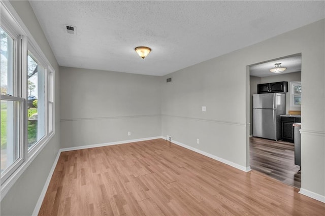 2411 NE 60th St, Gladstone, MO 64118 - empty room featuring a textured ceiling, light wood finished floors, baseboards, and visible vents