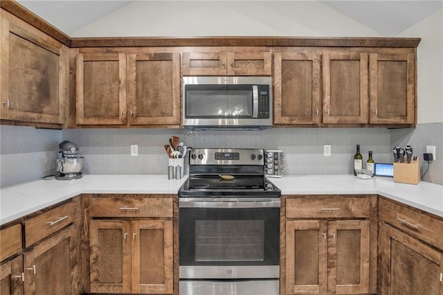 12631 Fountain Lake Cir, Grandview, MO 64030 - kitchen featuring appliances with stainless steel finishes, vaulted ceiling, brown cabinets, backsplash, and light countertops